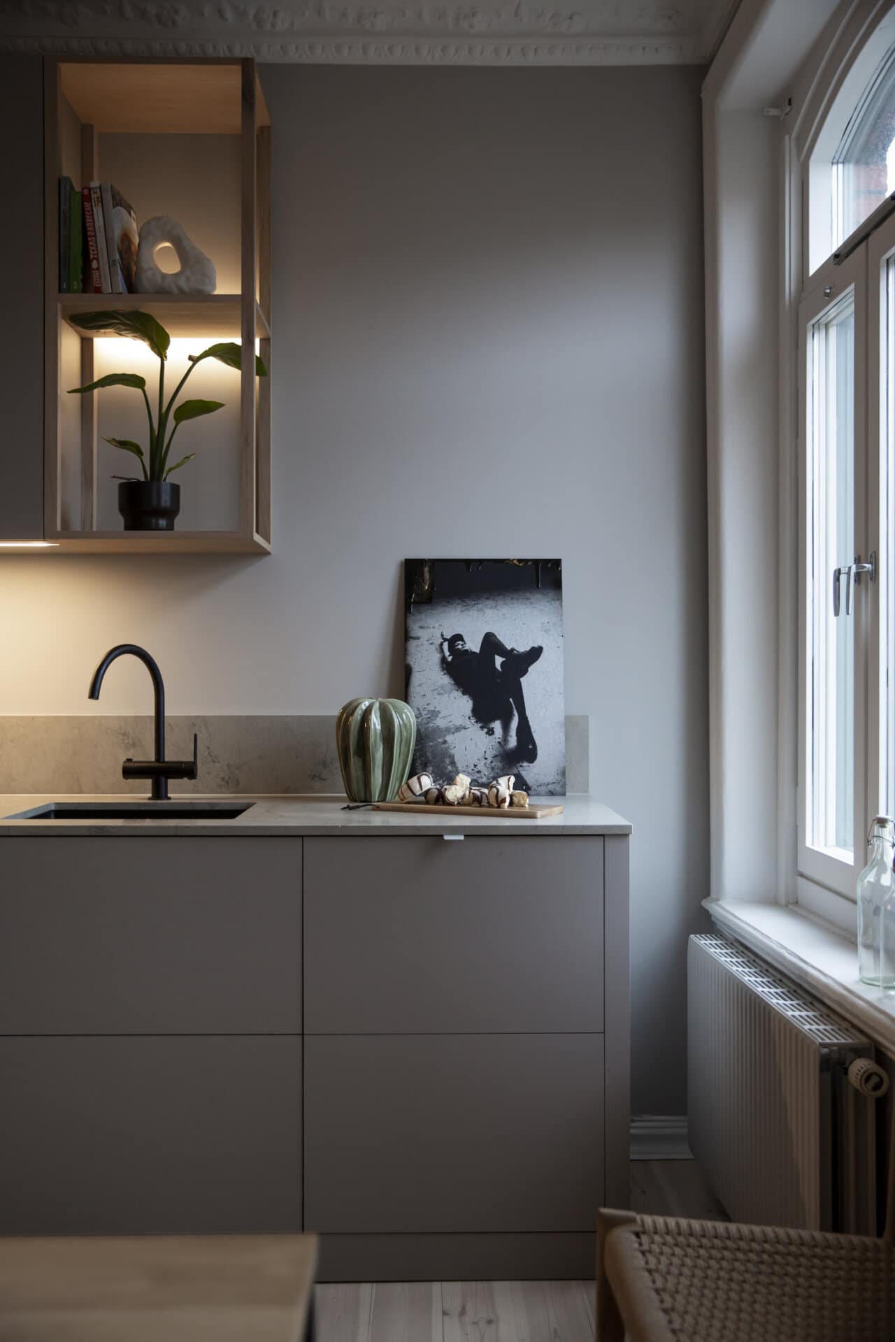 Stiligt - Modernt kök med stiligt minimalistisk design. Har en svart kran, krukväxt, inramade siluettkonstverk på disken, dekorativ vas och ett stort fönster.