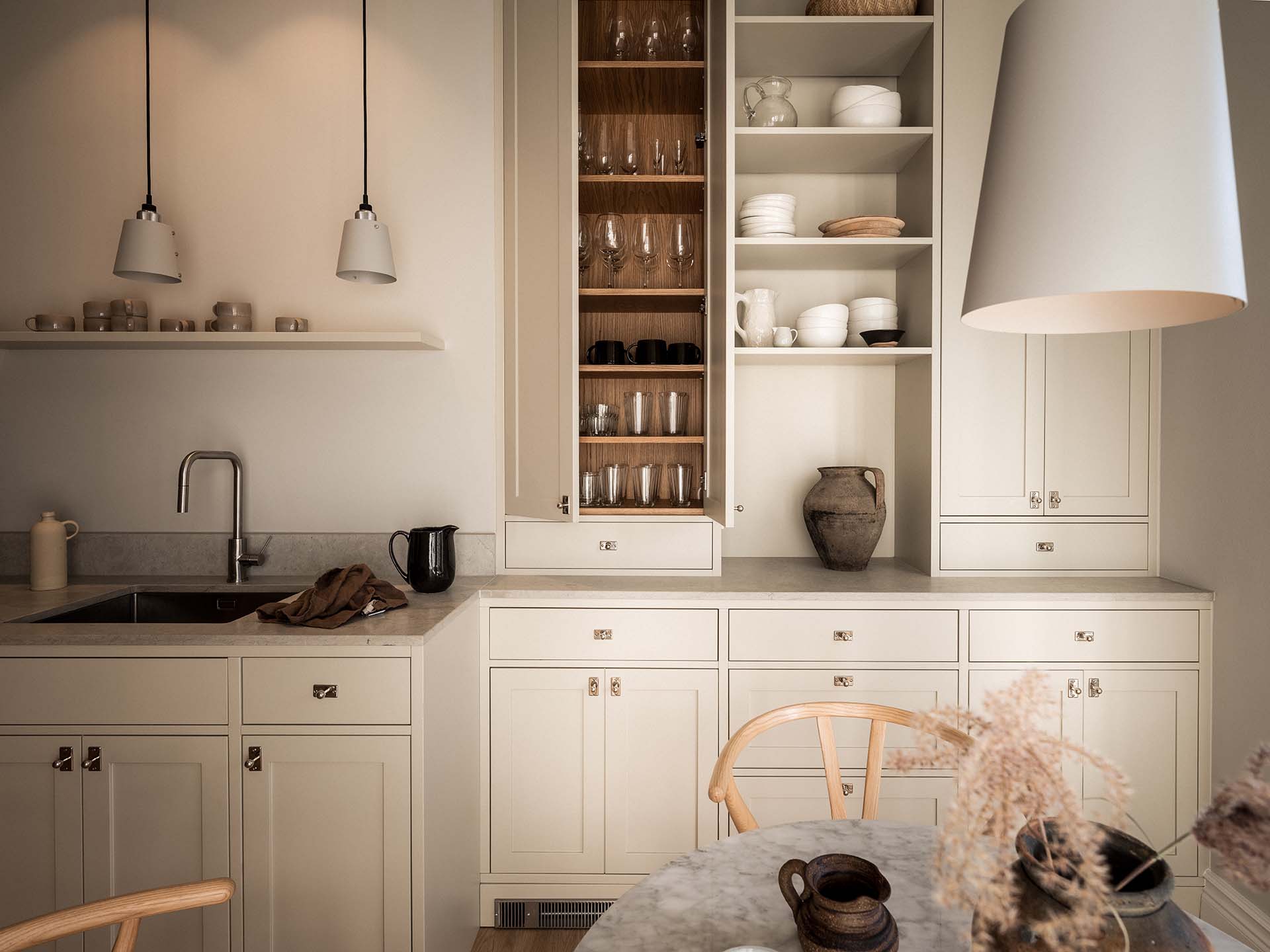 Stiligt - Ett stiligt modernt kök har beige skåp, öppna hyllor med porslin och en bänkskiva i marmor. Ett handfat, en vattenkokare och olika dekorativa föremål bidrar till den chica atmosfären.