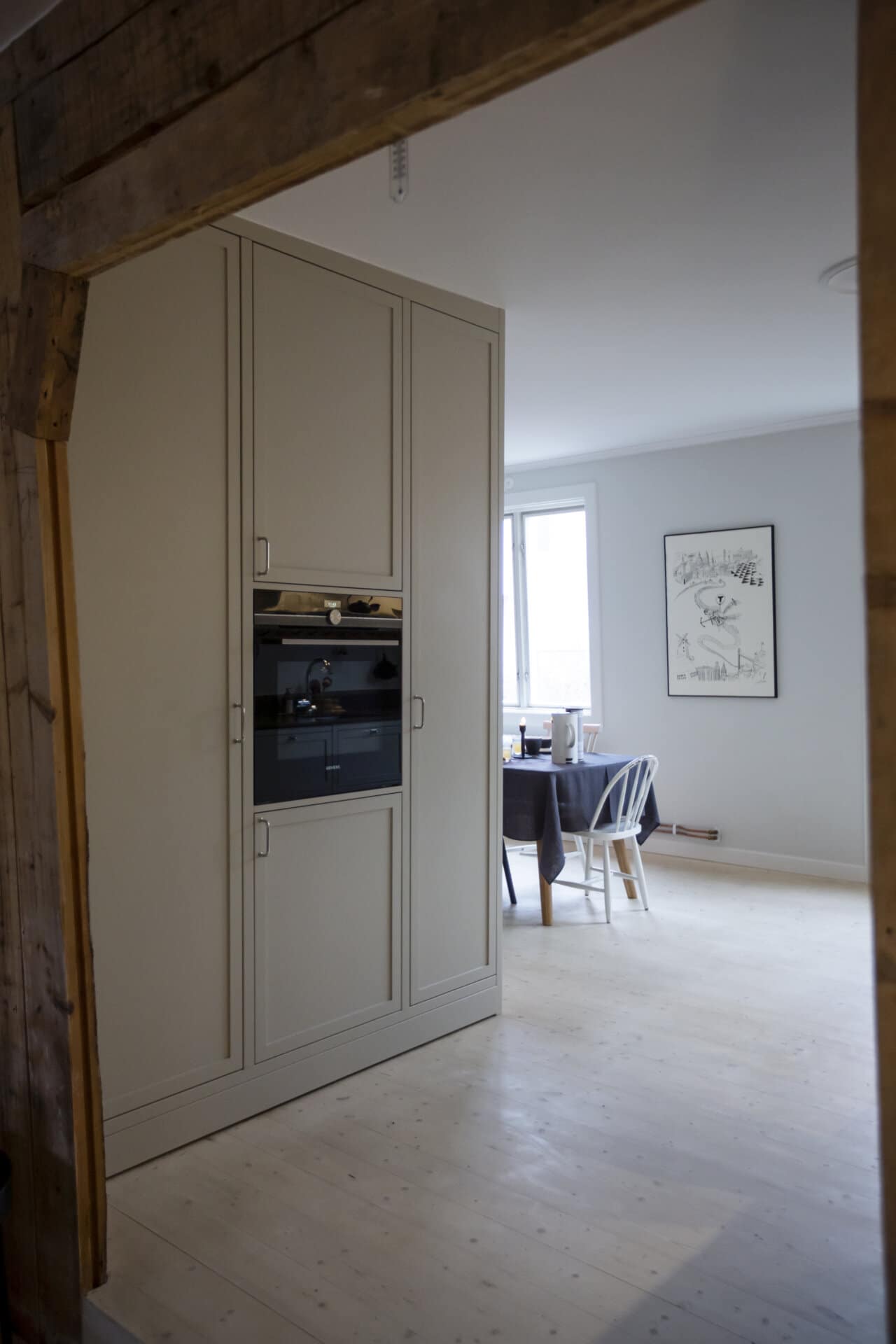 Stiligt - Klassiskt shakerkök med en inbyggd ugn och snygga skåp, kompletterat med en matplats där ett elegant bord och stolar sitter under ett elegant väggkonstverk.