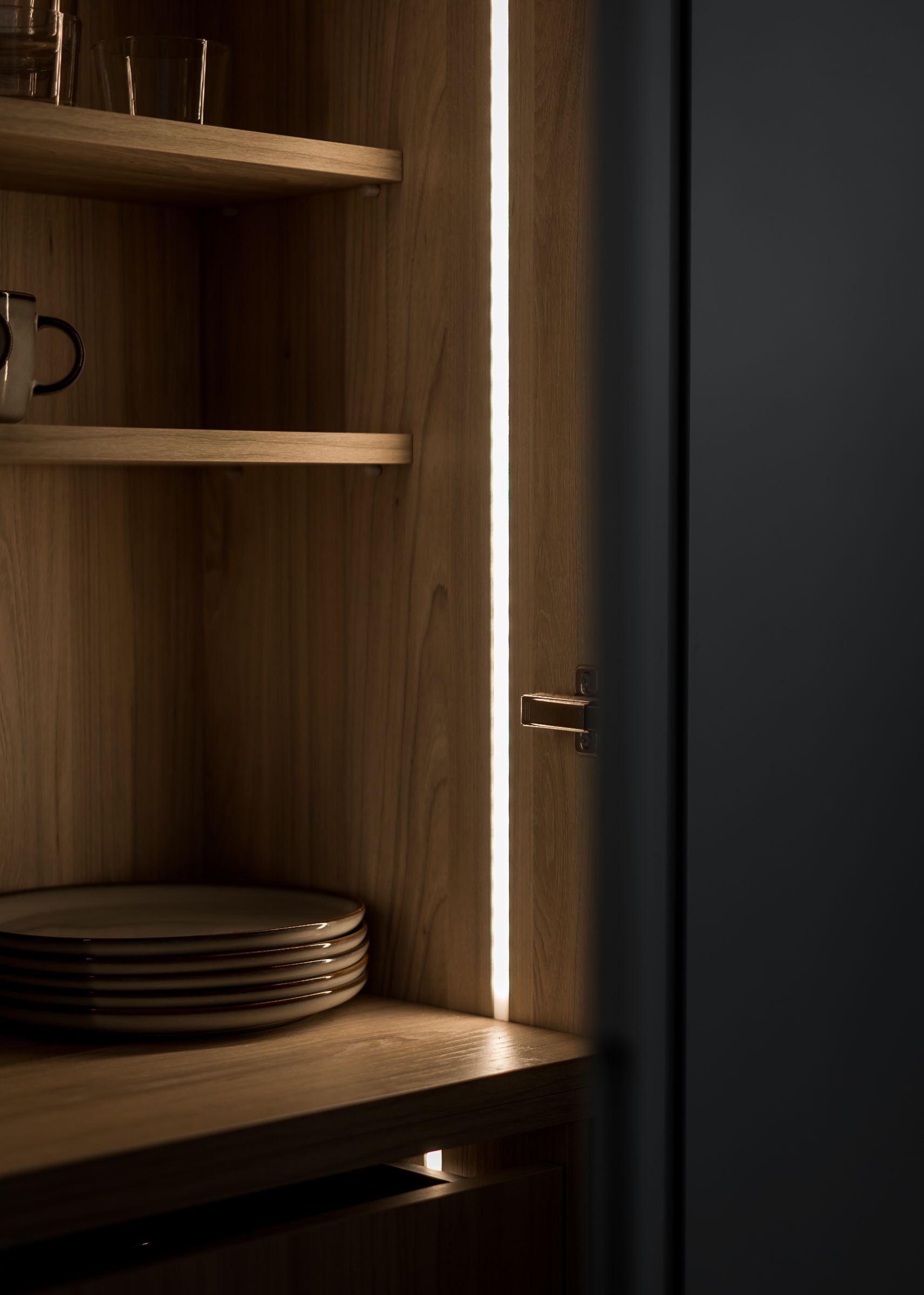 Stiligt - Stiligt köksskåp i trä med invändig belysning, elegant utställningshyllor prydda med tallrikar, koppar och glas.