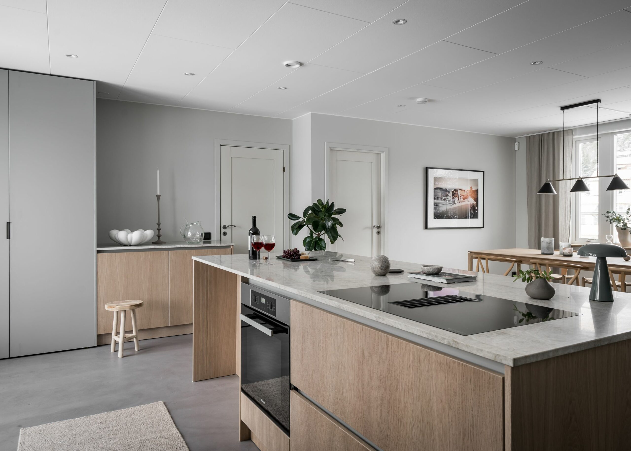 Stiligt - Ett modernt kök och matplats har stiligt design med träskåp, bänkskivor i marmor, spishäll, vin, fruktskål och taklampor som lyser upp matbordet. Neutrala toner och minimalistisk inredning förstärker den eleganta atmosfären.