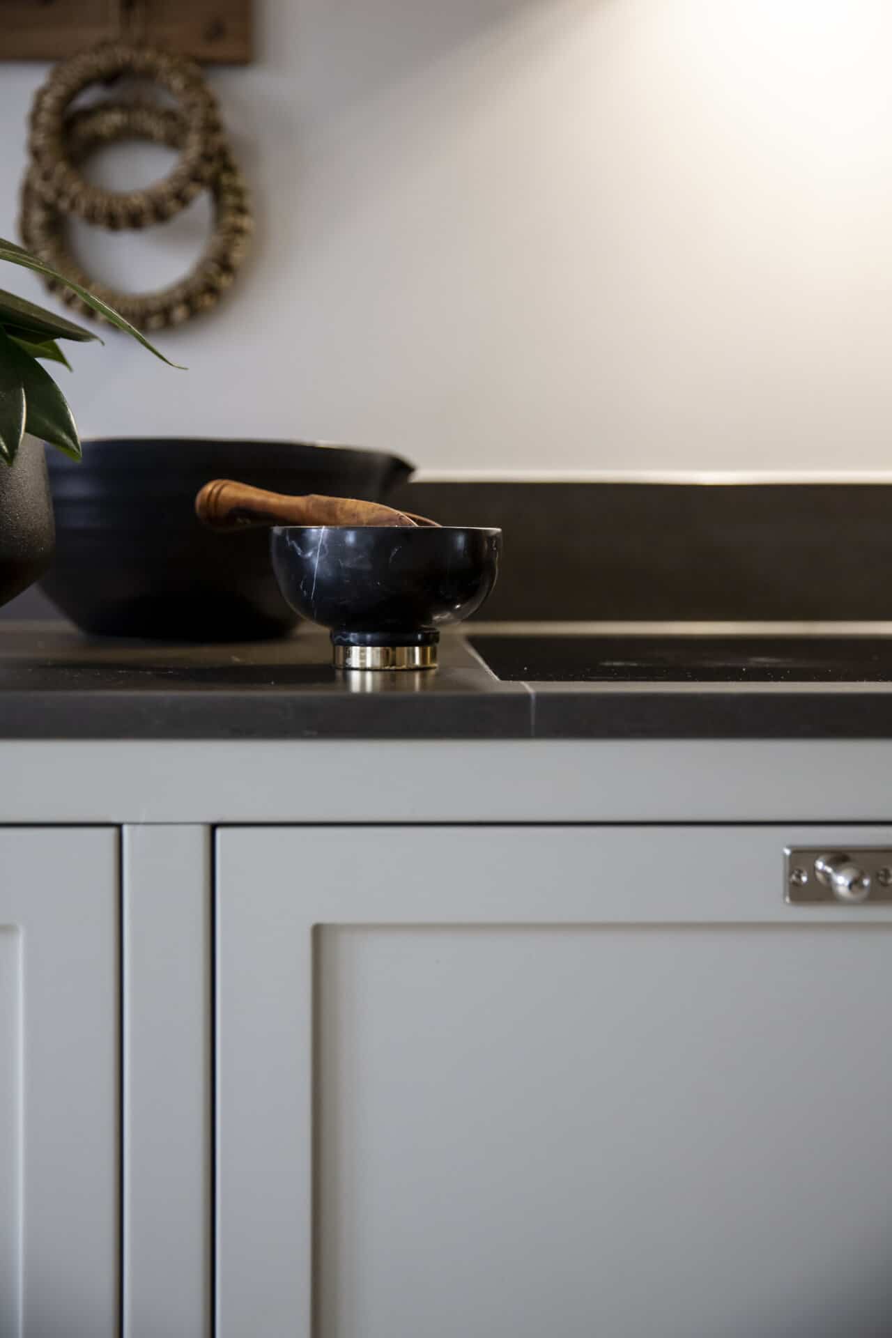 Stiligt - En stiligt svart skål med en trästöt vilar på en mörk köksbänk nära ett grått skåp, medan en elegant svart kruka och vävda ringar subtilt kompletterar scenen i bakgrunden.