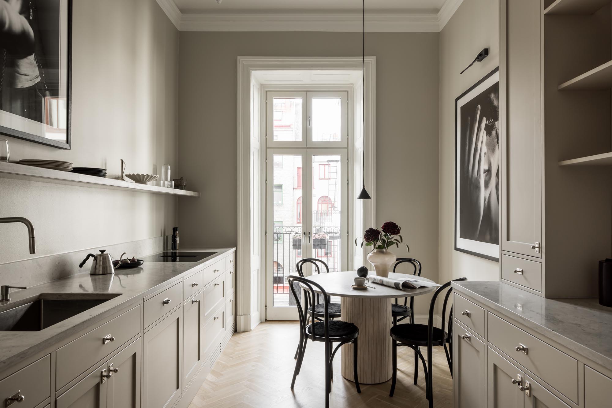 Stiligt - Ett stiligt minimalistiskt kök har ljusa skåp, ett runt bord för två och svarta stolar mot en bakgrund av svartvita konstverk som pryder väggarna. Fönstervyn förstärker detta eleganta utrymme.